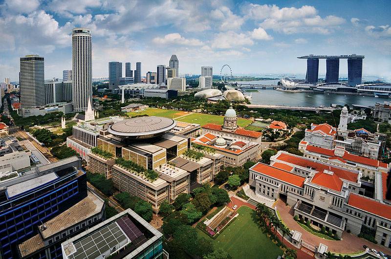 An aerial view of the Civic District of Singapore. The buildings visible include the Supreme Court of Singapore (centre left, with disc), the Old Supreme Court Building (centre right, with dome), and Parliament House (right, with orange roof). In the background are the three towers of the Marina Bay Sands Hotel. Photo by William Cho.