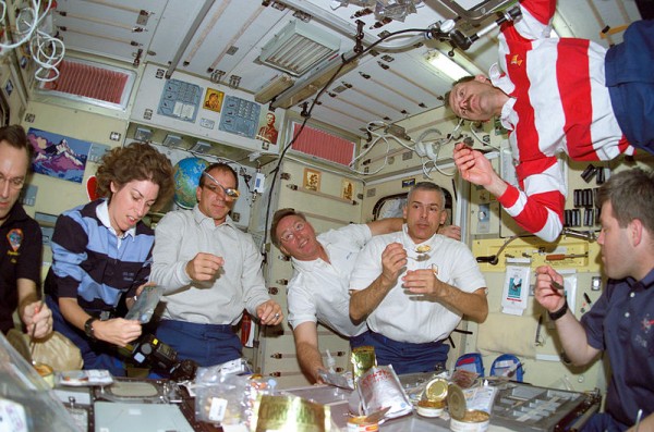 The Expedition Four and STS-110 crewmembers share a meal in the Zvezda Service Module on the International Space Station (ISS). Photo by NASA.
